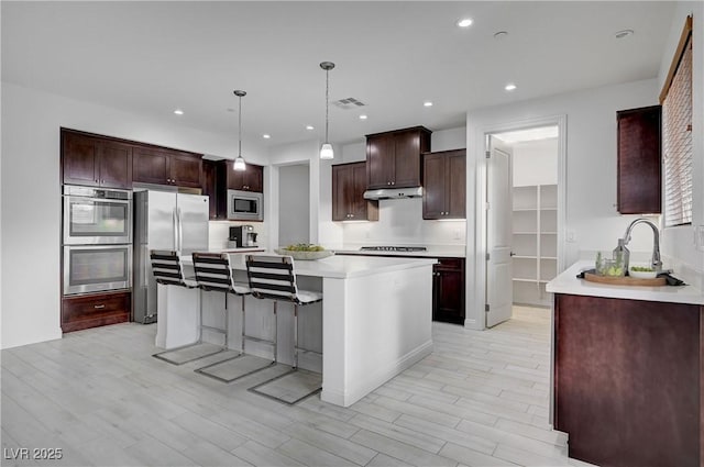 kitchen featuring visible vents, light wood-style flooring, light countertops, under cabinet range hood, and appliances with stainless steel finishes