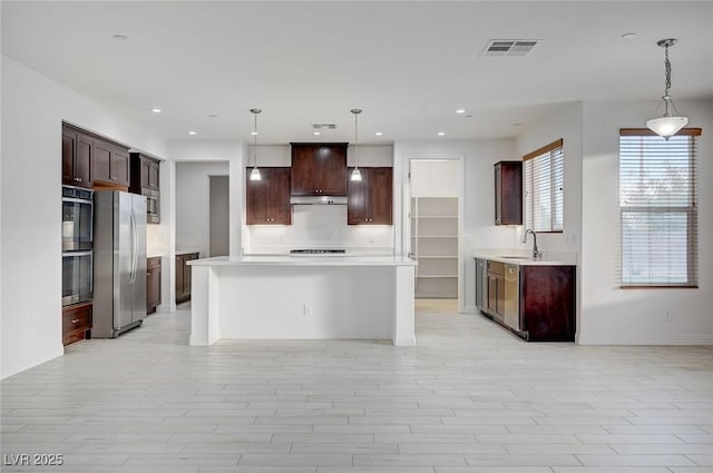 kitchen with visible vents, a sink, stainless steel appliances, light countertops, and a center island