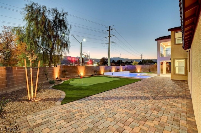 yard at dusk with a patio area, a fenced backyard, and a balcony