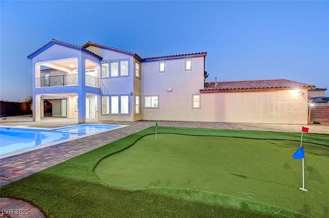 back of property with a balcony, a pool with connected hot tub, stucco siding, a tile roof, and a patio area