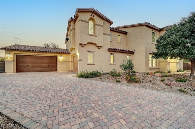 mediterranean / spanish home with stucco siding, a tiled roof, decorative driveway, and a garage