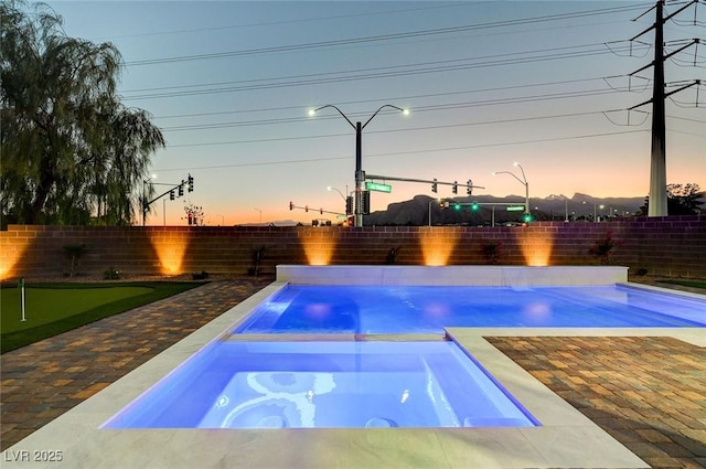 pool at dusk featuring a patio area, a fenced backyard, and a pool with connected hot tub