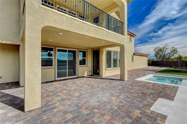 view of patio featuring fence, a balcony, and a hot tub