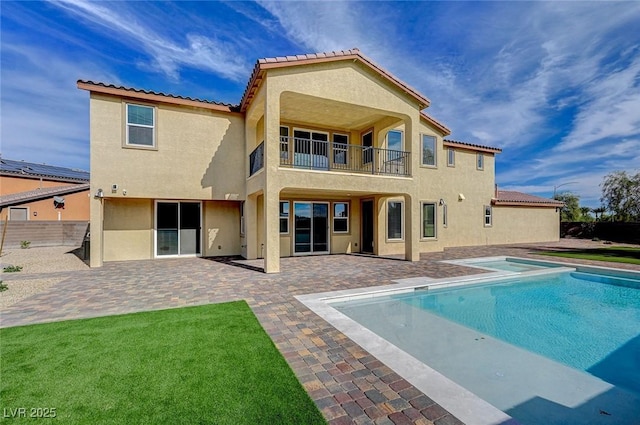 rear view of property with a balcony, fence, an in ground hot tub, stucco siding, and a patio area