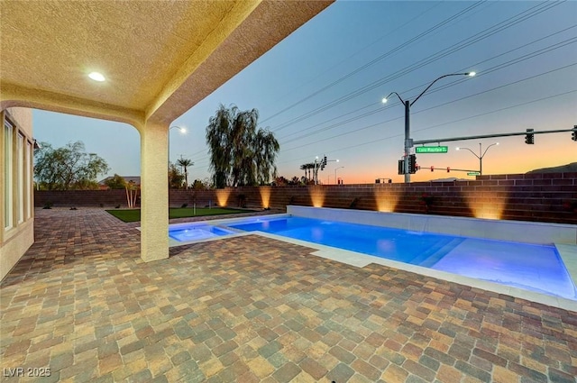 pool at dusk with a patio area, a fenced in pool, and a fenced backyard