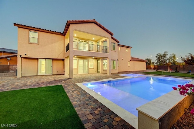 rear view of property with stucco siding, a lawn, a fenced backyard, a balcony, and a patio area