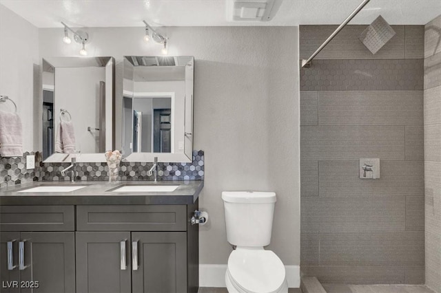 bathroom with tiled shower, vanity, toilet, and decorative backsplash