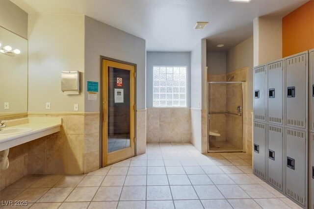 bathroom with walk in shower, sink, tile patterned flooring, and tile walls