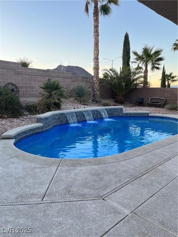 pool at dusk featuring pool water feature