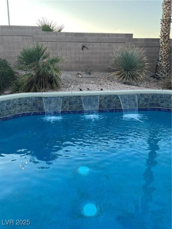 pool at dusk featuring pool water feature