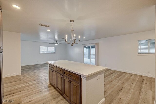 kitchen with pendant lighting, ceiling fan with notable chandelier, a center island, and light wood-type flooring