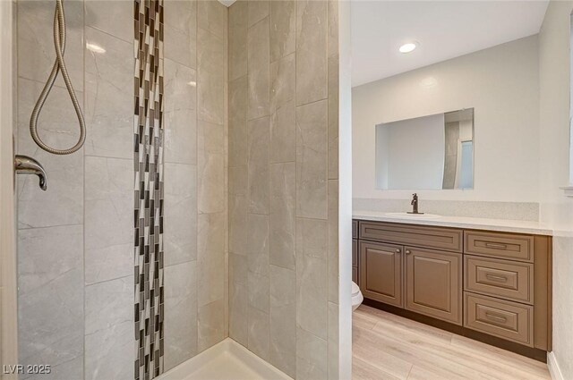 bathroom featuring a tile shower, vanity, hardwood / wood-style flooring, and toilet