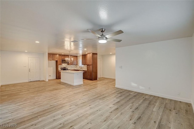 unfurnished living room with ceiling fan with notable chandelier and light hardwood / wood-style flooring