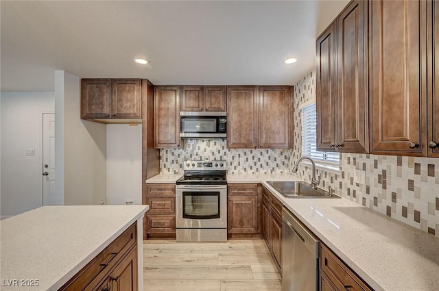 kitchen with sink, light wood-type flooring, tasteful backsplash, light stone counters, and stainless steel appliances