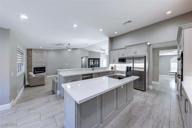 kitchen with light stone countertops, a center island, stainless steel appliances, kitchen peninsula, and a fireplace