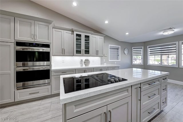 kitchen featuring black electric stovetop, vaulted ceiling, double oven, tasteful backsplash, and a kitchen island