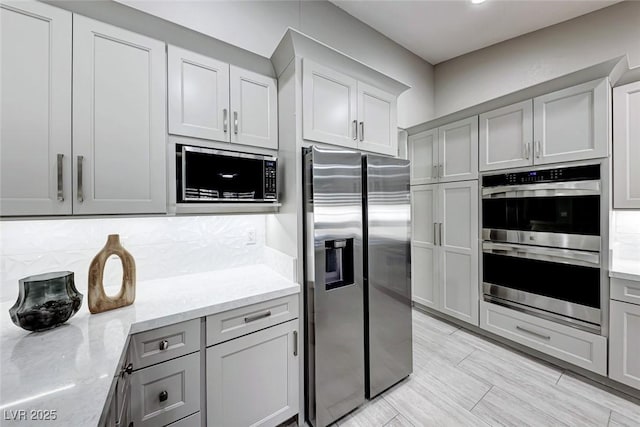 kitchen with tasteful backsplash, gray cabinetry, light stone countertops, and appliances with stainless steel finishes