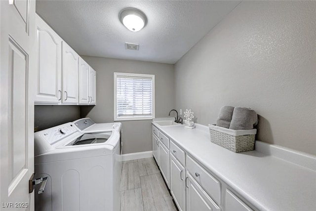 laundry room with cabinets, a textured ceiling, washer and dryer, and sink