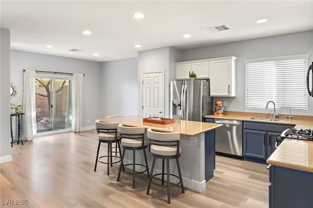 kitchen featuring appliances with stainless steel finishes, blue cabinets, sink, white cabinets, and a center island