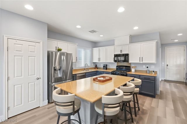 kitchen featuring a breakfast bar, sink, black appliances, white cabinets, and a center island