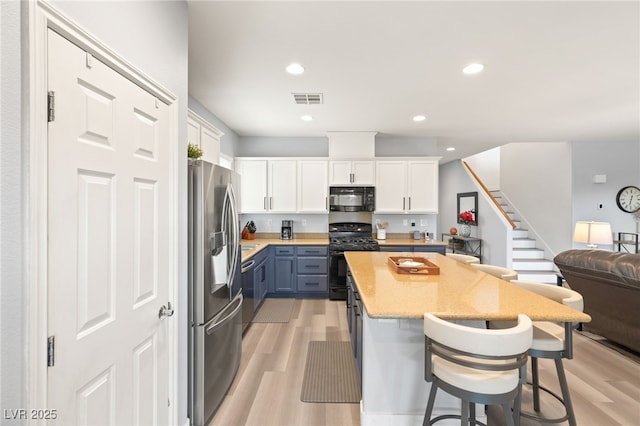 kitchen with black appliances, a kitchen breakfast bar, white cabinets, blue cabinets, and light hardwood / wood-style flooring