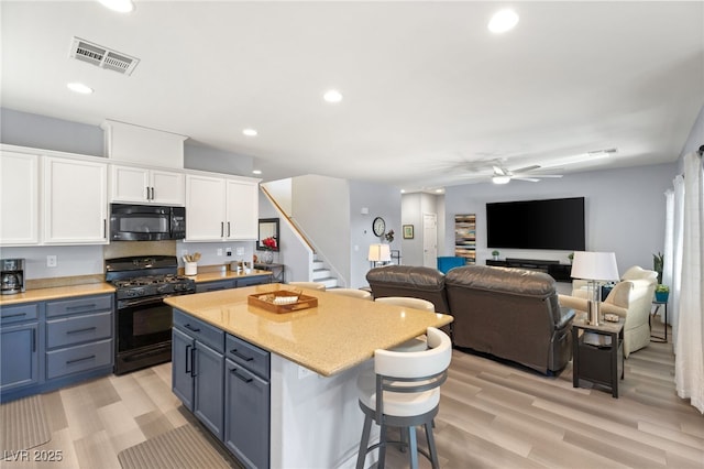 kitchen featuring white cabinetry, ceiling fan, a kitchen bar, a kitchen island, and black appliances