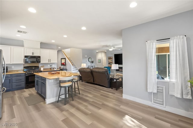 kitchen with ceiling fan, black appliances, white cabinets, a center island, and a breakfast bar area