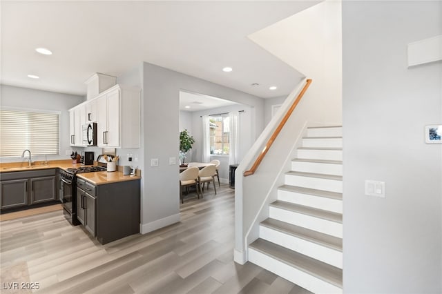 kitchen featuring white cabinets, black gas range oven, light wood-type flooring, and sink