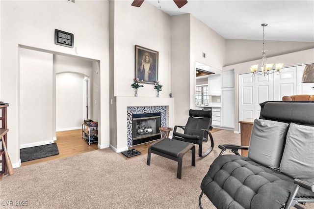 carpeted living room featuring ceiling fan with notable chandelier, high vaulted ceiling, and a tiled fireplace