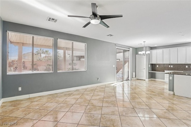 unfurnished living room with light tile patterned floors, ceiling fan with notable chandelier, and a healthy amount of sunlight