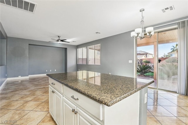 kitchen with white cabinetry, hanging light fixtures, dark stone counters, a kitchen island, and ceiling fan with notable chandelier