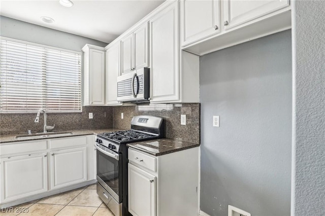 kitchen featuring dark stone counters, stainless steel appliances, sink, light tile patterned floors, and white cabinets