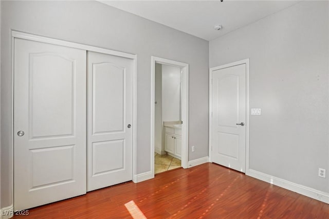 unfurnished bedroom featuring hardwood / wood-style flooring, ensuite bath, and a closet