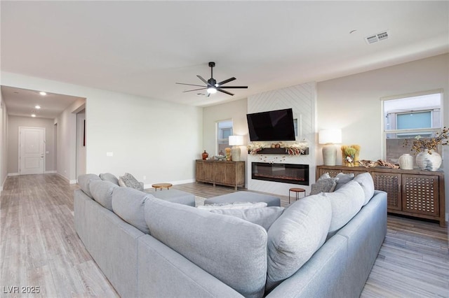 living room with ceiling fan, a large fireplace, and light wood-type flooring