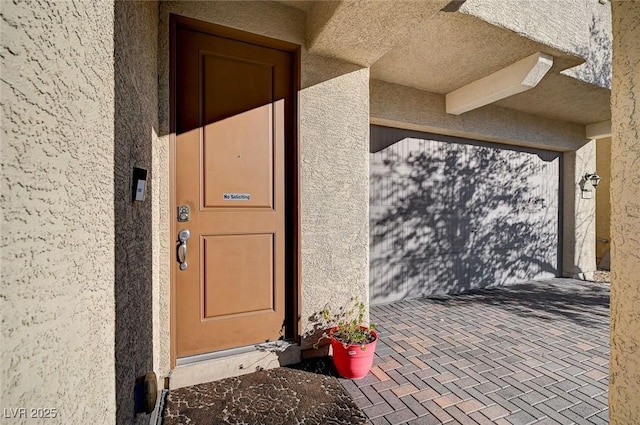 view of exterior entry with a garage and stucco siding