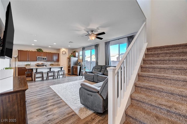 living area with light wood-type flooring, ceiling fan, recessed lighting, and stairs