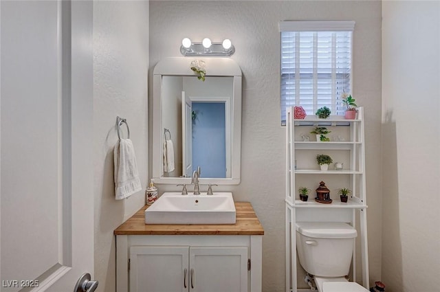 bathroom featuring a textured wall, vanity, and toilet