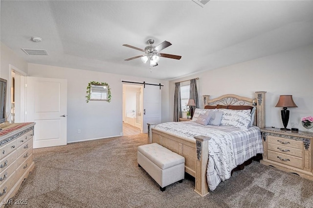 bedroom with carpet floors, visible vents, a barn door, a ceiling fan, and connected bathroom