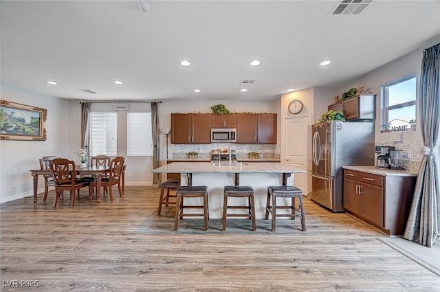 kitchen featuring visible vents, decorative backsplash, appliances with stainless steel finishes, light wood-style floors, and an island with sink