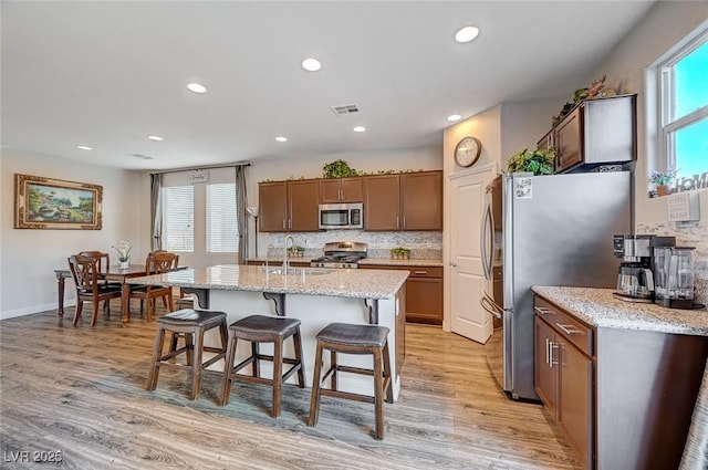 kitchen featuring visible vents, a kitchen breakfast bar, appliances with stainless steel finishes, light stone countertops, and an island with sink