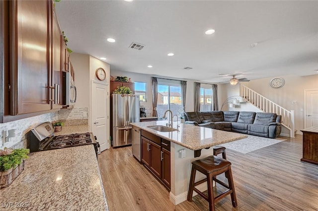 kitchen with stainless steel appliances, visible vents, open floor plan, a sink, and an island with sink