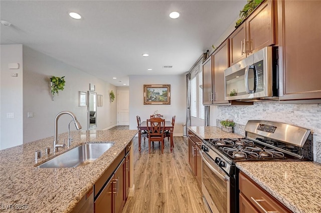 kitchen featuring appliances with stainless steel finishes, brown cabinetry, a sink, and light stone counters