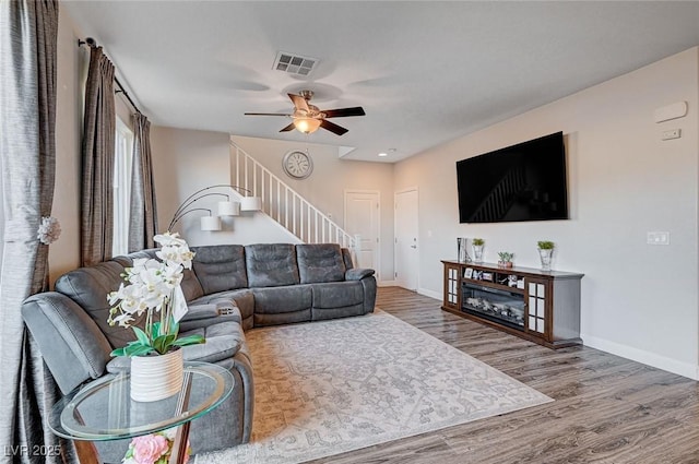 living room with stairs, wood finished floors, visible vents, and baseboards