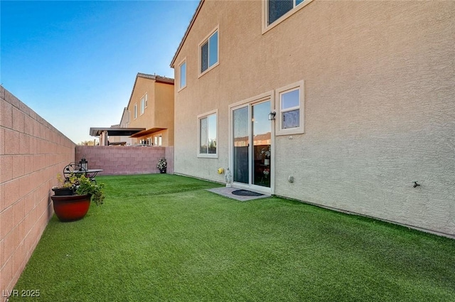 rear view of property with a fenced backyard, a lawn, and stucco siding