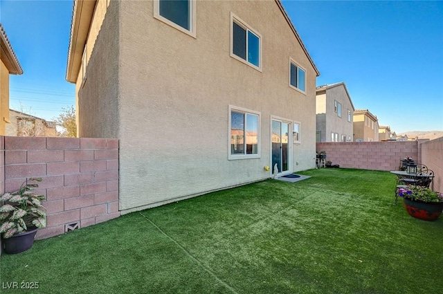 back of house with a fenced backyard, a yard, and stucco siding