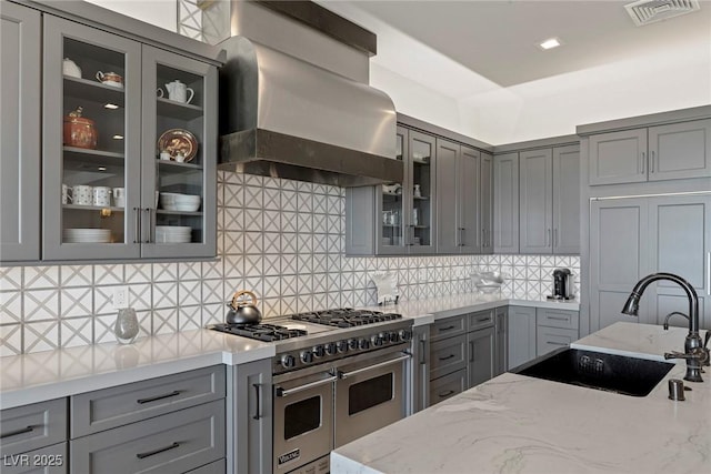 kitchen with gray cabinetry, double oven range, sink, wall chimney exhaust hood, and light stone countertops