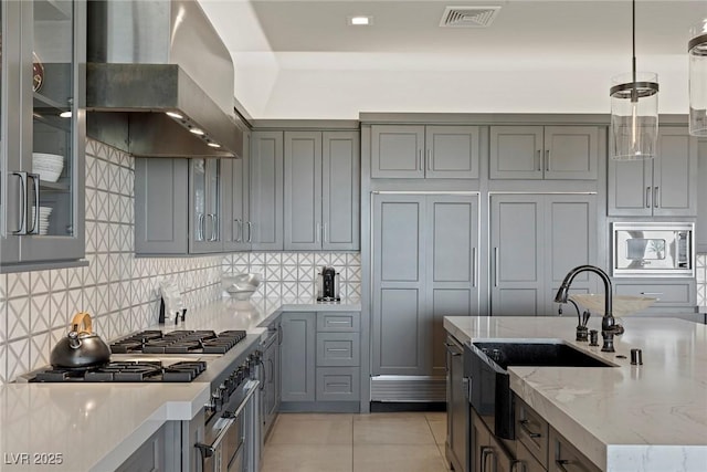 kitchen featuring light stone countertops, stainless steel microwave, wall chimney exhaust hood, decorative light fixtures, and light tile patterned floors