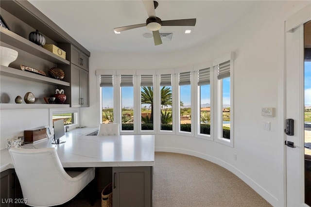 carpeted home office featuring built in shelves, ceiling fan, and built in desk