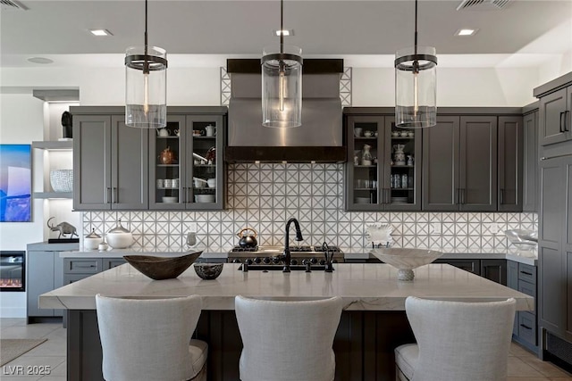 kitchen with light stone countertops, wall chimney range hood, backsplash, pendant lighting, and light tile patterned floors