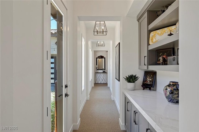 corridor featuring light colored carpet and an inviting chandelier